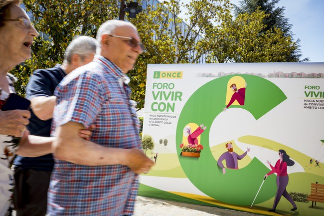 Un hombre con gafas de sol ante el cartel de Vivir con C, exterior