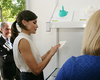 La Reina Letizia toca las siglas ONCE en relieve en un papel que ella escribió en tinta, durante su visita al estand de la ONCE 