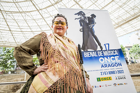 La artista ciega Rocío López posa junto al cartel de la 17 Bienal de Música ONCE