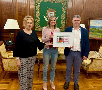 Responsables de la ONCE en Navarra entregan a Cristina Ibarrola una lámina enmarcada con el cupón dedicado a la Fiesta de San Fermín