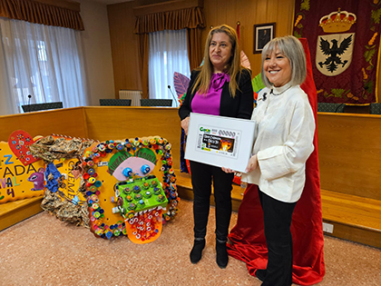 Araceli de las Heras y María José Ortega sostienen una lámina enmarcada con el cupón dedicado al Carnaval de la Galleta de Aguilar de Campoo