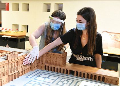 Una persona con discapacidad visual toca una maqueta, junto a una guía del museo, ataviada con mascarilla, máscara y guantes