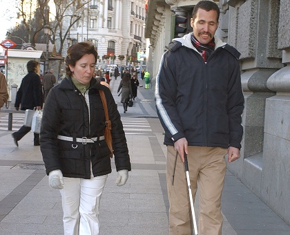 Una técnico de rehabilitación de la ONCE enseña a usar el bastón blanco a una persona extranjera