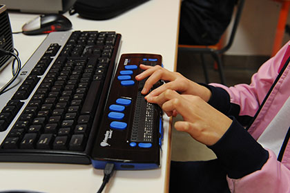 Manos de una niña ciega utilizando una línea braille
