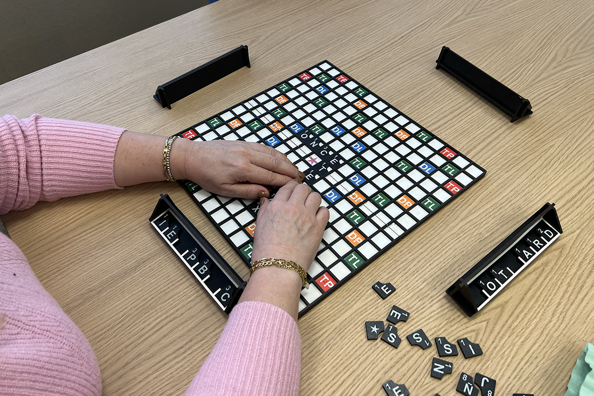 Persona con discapacidad visual tocando el tablero y la fichas en relieve del juego Apalabrados