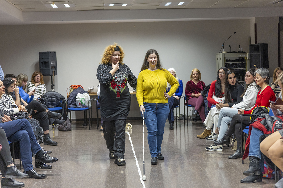 Una mujer ciega con el bastón blanco recibiendo las indicaciones para desfilar durante el ensayo