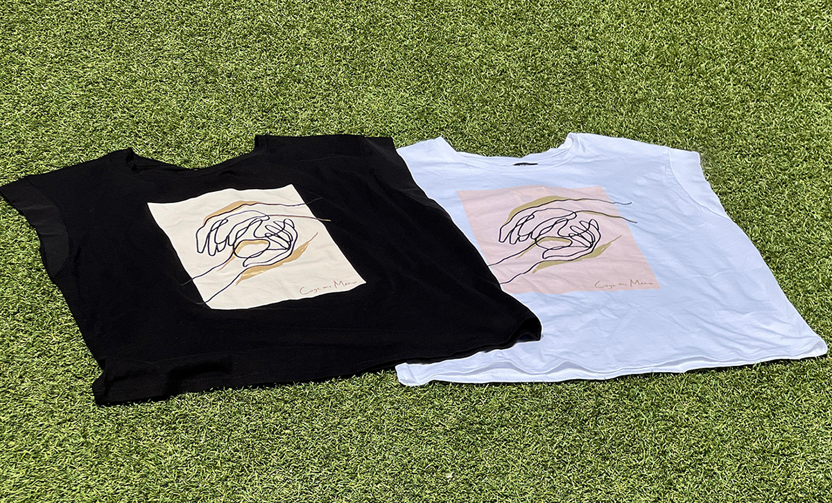 Los dos modelos de camiseta de Sfera con la imagen de dos manos cogiéndose y el lema "Coge mi mano". Una camiseta es blanca y otra es negra y la silueta de las manos está en relieve