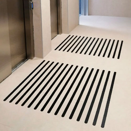 Pavimento podotáctil de líneas paralelas ante las puertas de ascensores